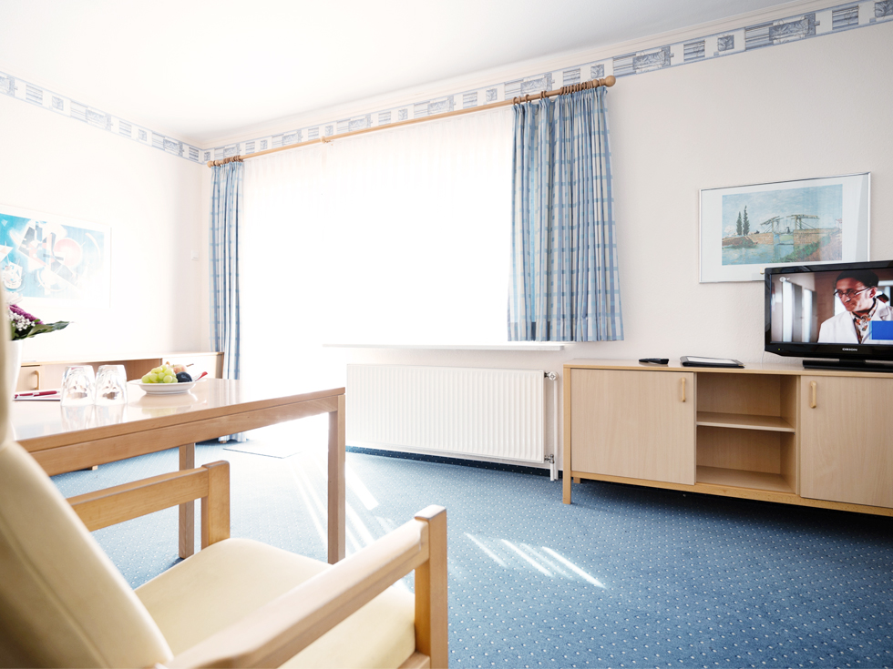 SoVD - helles Appartement mit blauem Teppich, Fernseher und Holzmöbeln