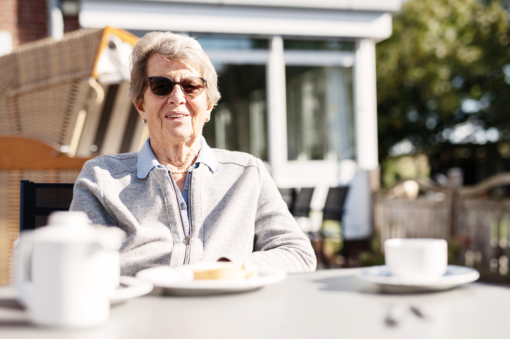 Seniorin auf der Terrasse am Tisch mit Kaffee und Kuchen