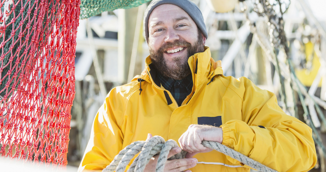 Fischer in gelber Jacke mit Mütze auf einem Kutter
